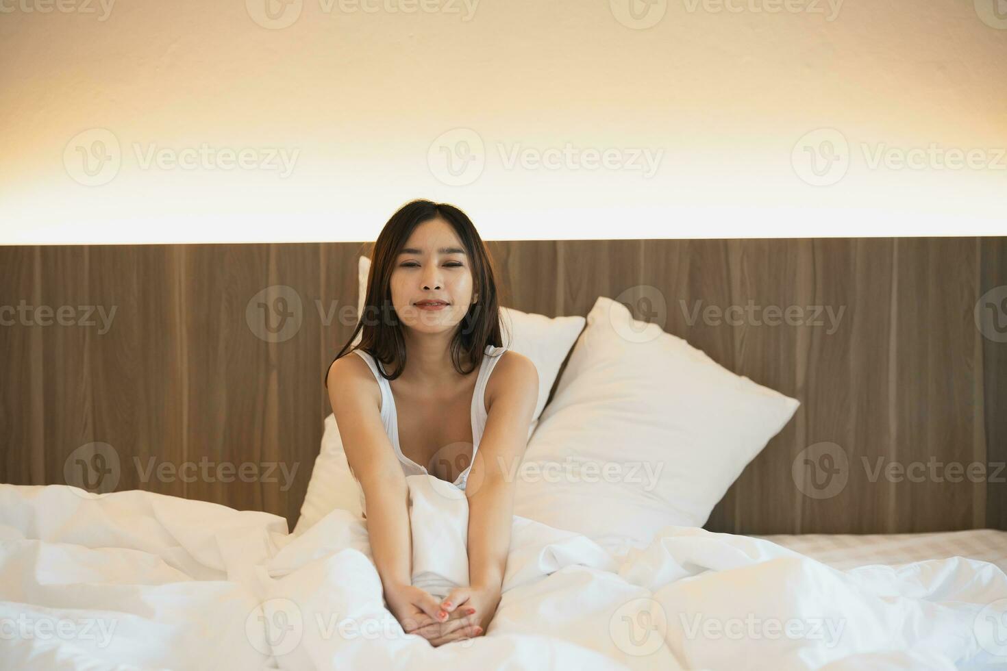 Asian woman laying on the bed, stretching and happy woman waking up in the morning after sleep, rest and relax at home. Resting, smile and stretch in bedroom, peaceful, cheerful comfortable concept. photo