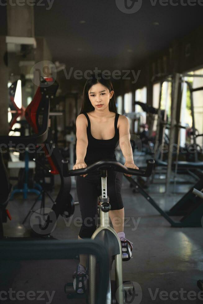 deportista asiática haciendo ejercicio en bicicleta en el gimnasio, la determinación de perder peso con cardio, la hace saludable. concepto de deporte de fitness de mujer de bicicleta de ejercicio. foto