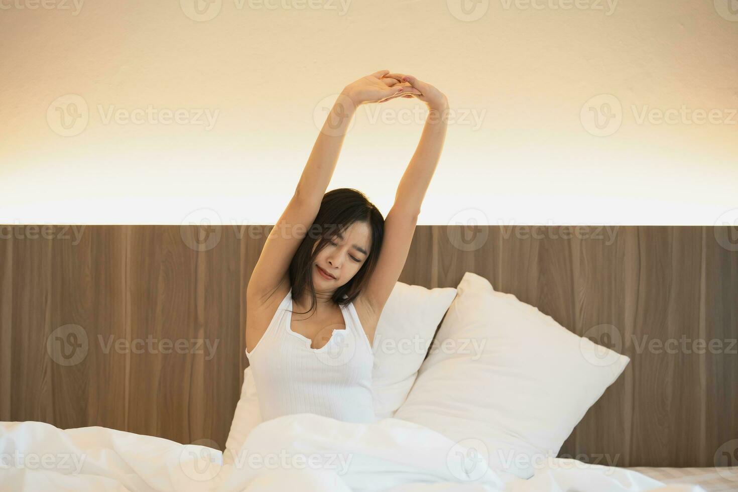 Asian woman laying on the bed, stretching and happy woman waking up in the morning after sleep, rest and relax at home. Resting, smile and stretch in bedroom, peaceful, cheerful comfortable concept. photo