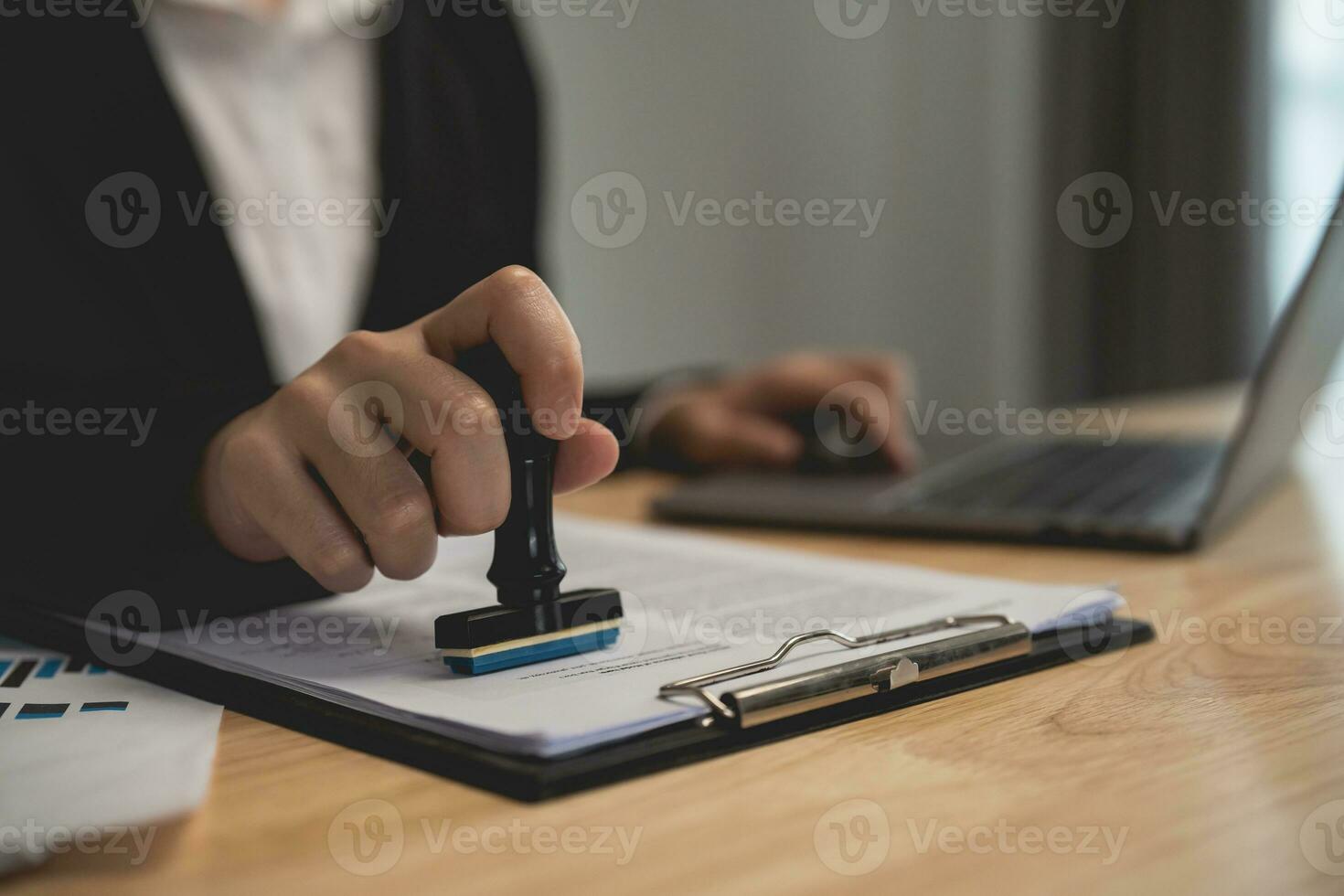 cerca arriba de mujer de negocios mano estampado con aprobado sello en documento a el oficina mesa, notario o negocio personas trabajo desde hogar. negocio trabajando o abogado concepto. foto