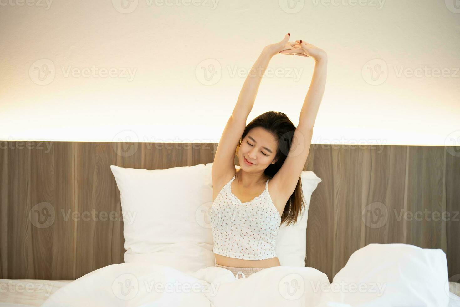 Asian woman laying on the bed, stretching and happy woman waking up in the morning after sleep, rest and relax at home. Resting, smile and stretch in bedroom, peaceful, cheerful comfortable concept. photo