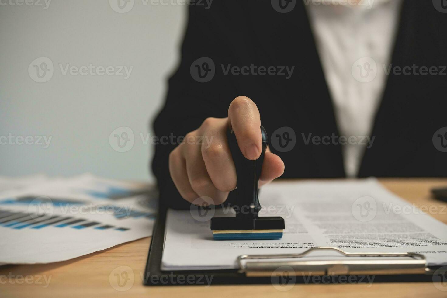 cerca arriba de mujer de negocios mano estampado con aprobado sello en documento a el oficina mesa, notario o negocio personas trabajo desde hogar. negocio trabajando o abogado concepto. foto