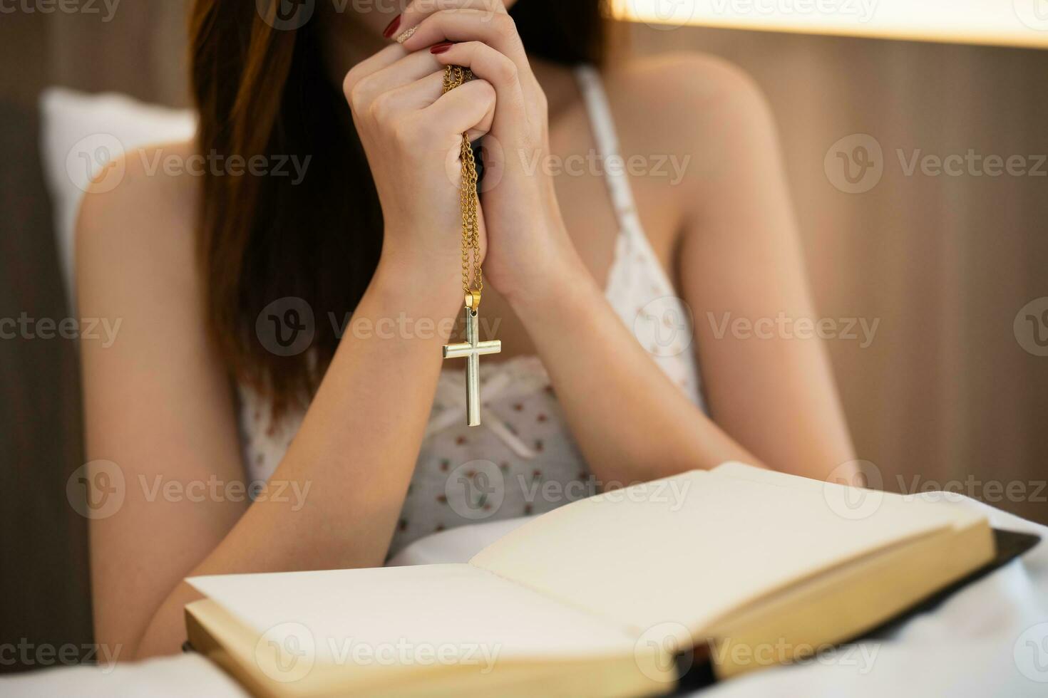 Asian woman doing hands together holding cross in prayer to God along with the bible Christian concept of faith, spirituality and religion, pray in the Bible. prayer bible on the bed in the bedroom. photo