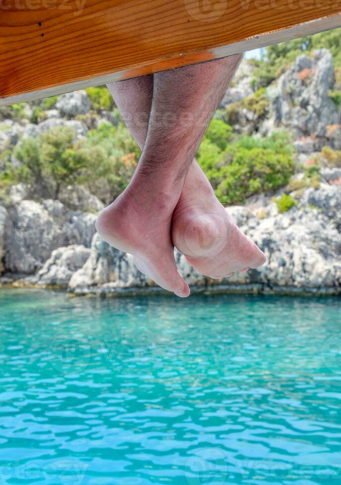 Bare feet hanging from wooden pier over sea water. Holiday vacation by the sea. photo