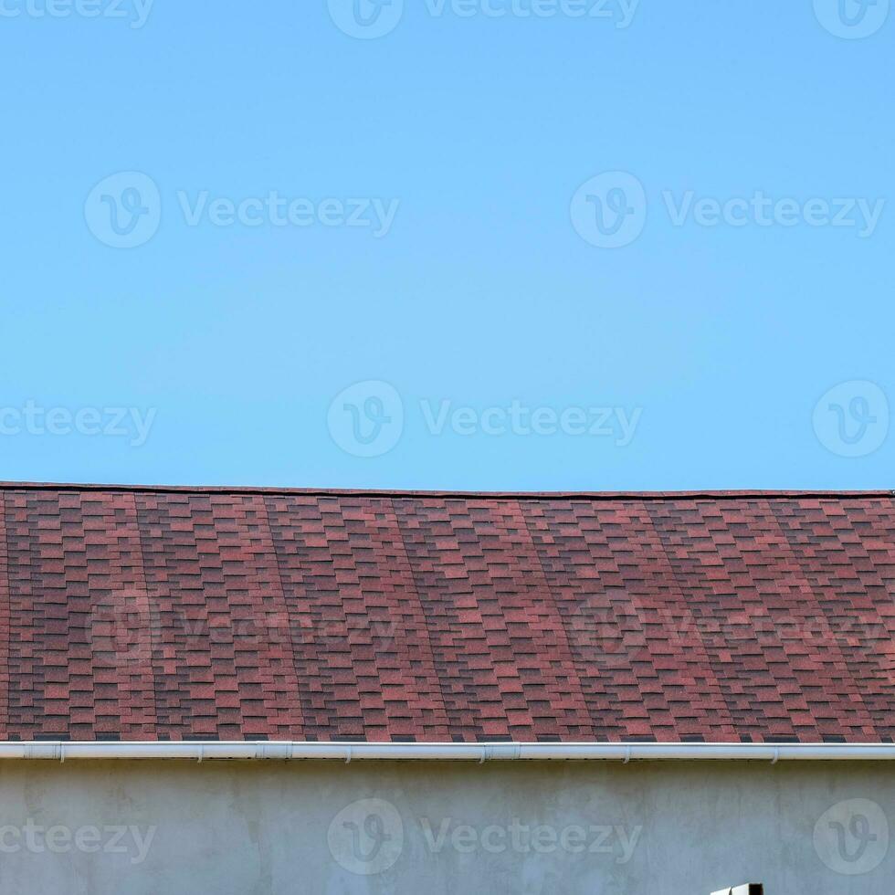 Roof from multi-colored bituminous shingles. Patterned bitumen shingles. Bituminous burgundy roof. photo