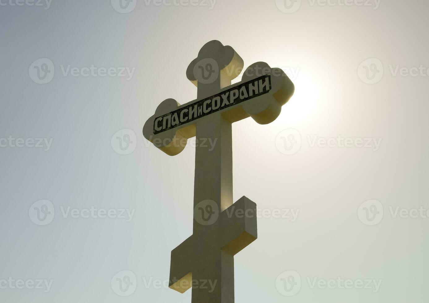 Orthodox cross against the blue sky and the sun. Cross in the ba photo