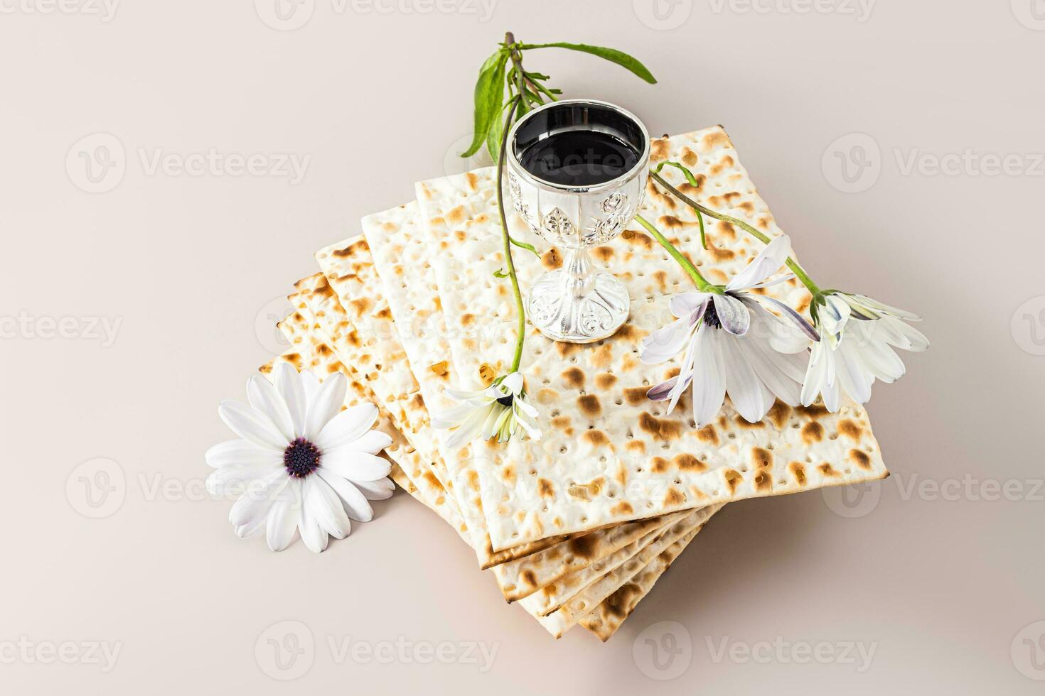 Concept of celebrating the Jewish holiday of Passover. A stack of matza and a silver cup with red wine and a delicate flower. Pastel background. photo