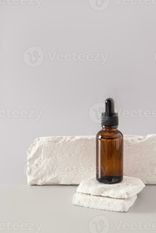 A classic cosmetic bottle with a dark glass pipette stands on two slices of white brick. Blank bottle mockup for product presentation. Vertical view. photo