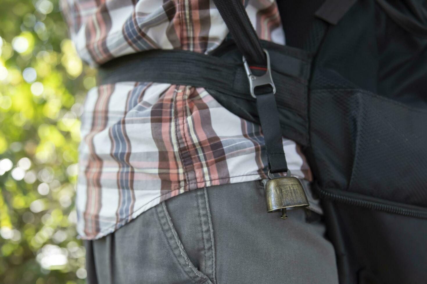 A person who wear a backpack with bear bell at the green forest in Autumn photo