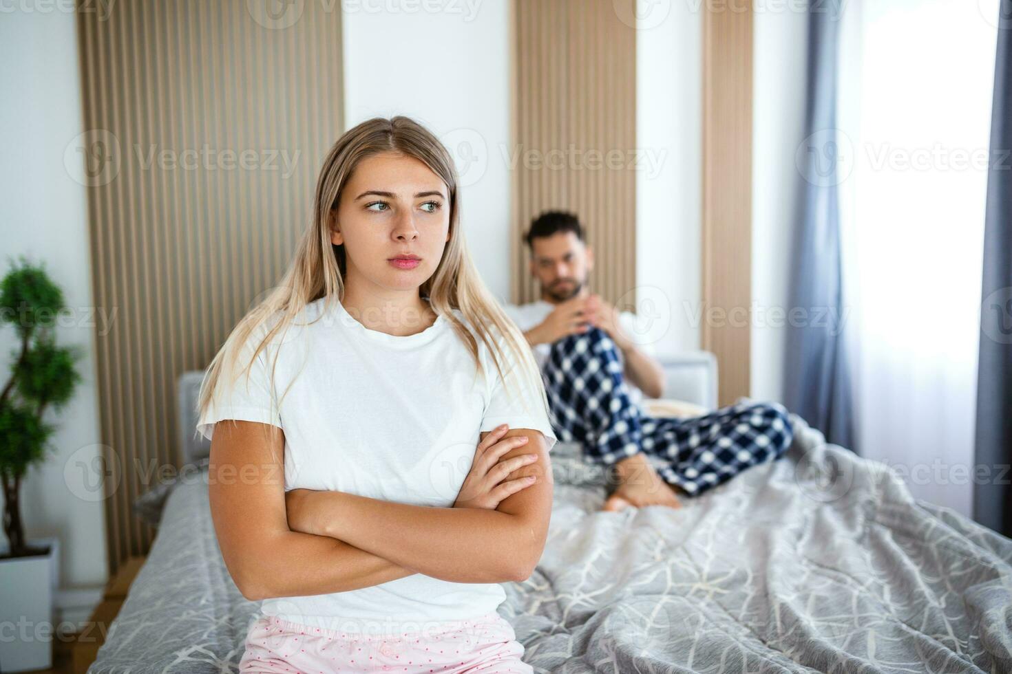 Upset Woman Sitting On The Bed With Man In The Background. Woman and man having a disagreement, Young couple in a bed bored woman photo