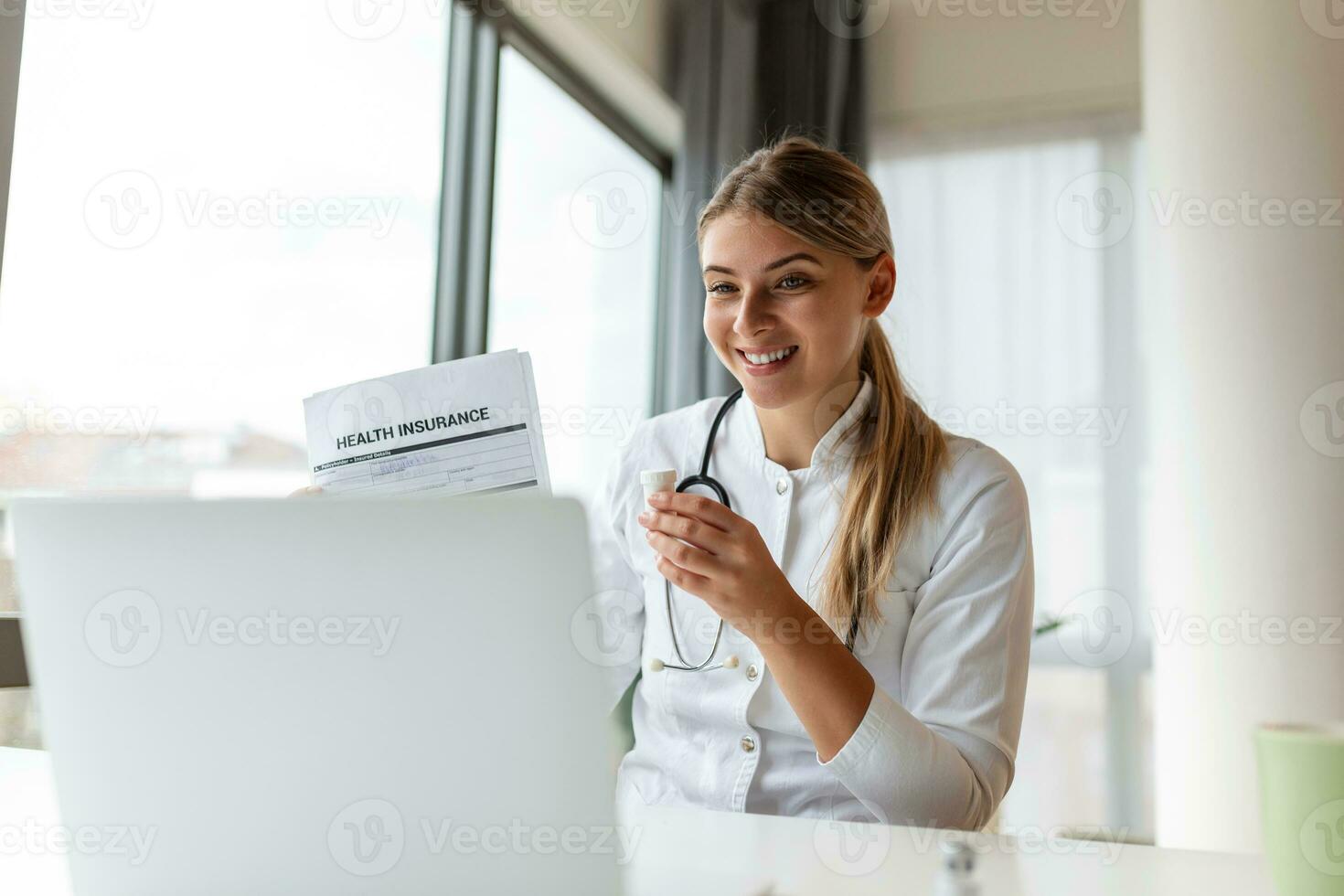 Attractive female doctor talking while explaining health insurance to patient through a video call with laptop in the consultation. photo