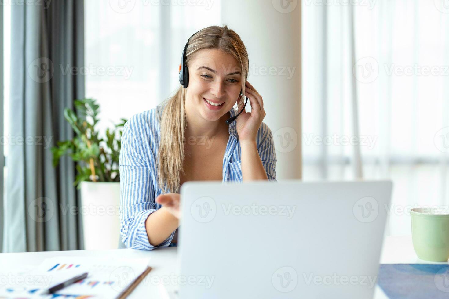 Happy young woman working on laptop while talking to customer on phone. Consulting corporate client in conversation with customer using computer. Service desk consultant talking in a call center. photo