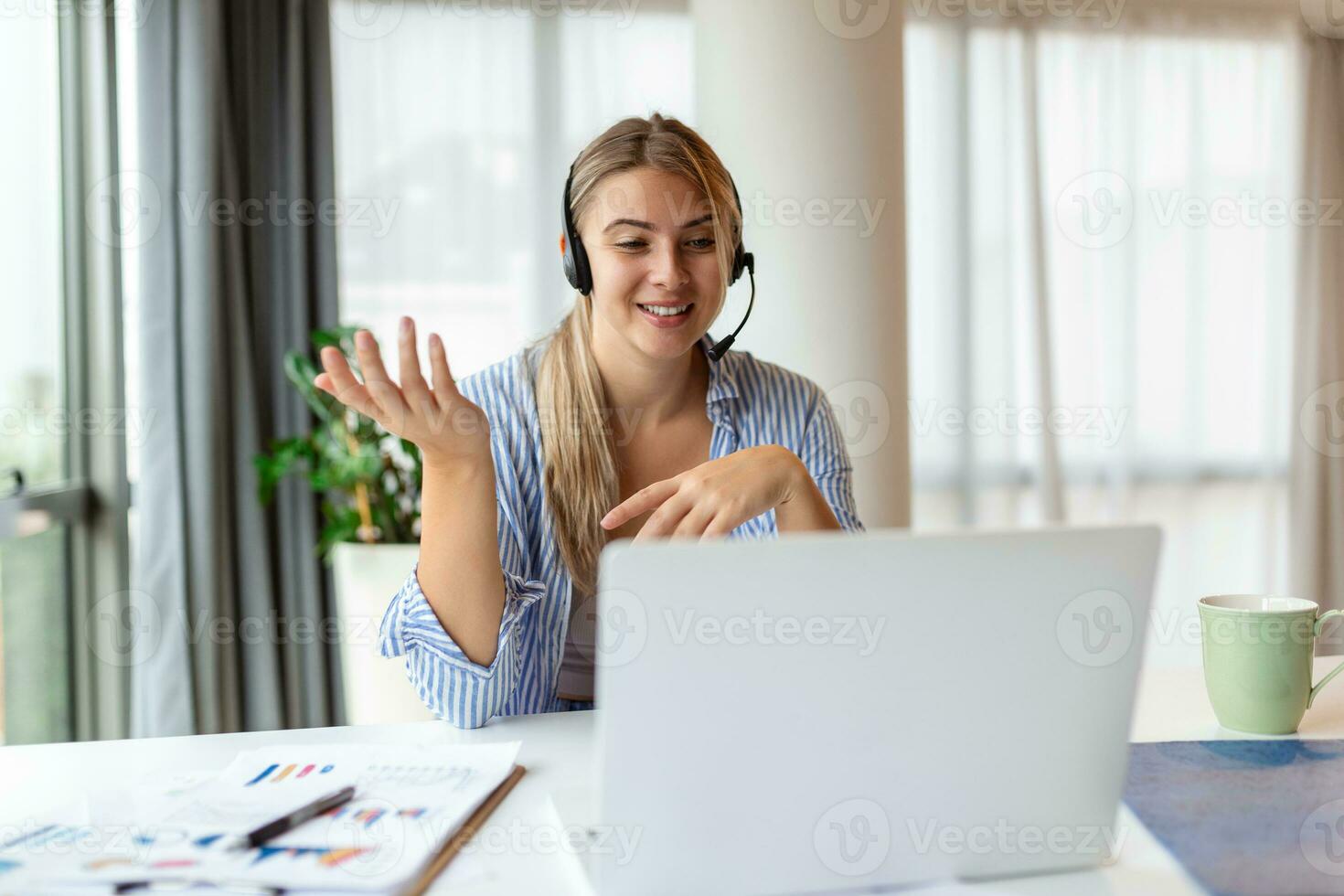 Happy young woman working on laptop while talking to customer on phone. Consulting corporate client in conversation with customer using computer. Service desk consultant talking in a call center. photo