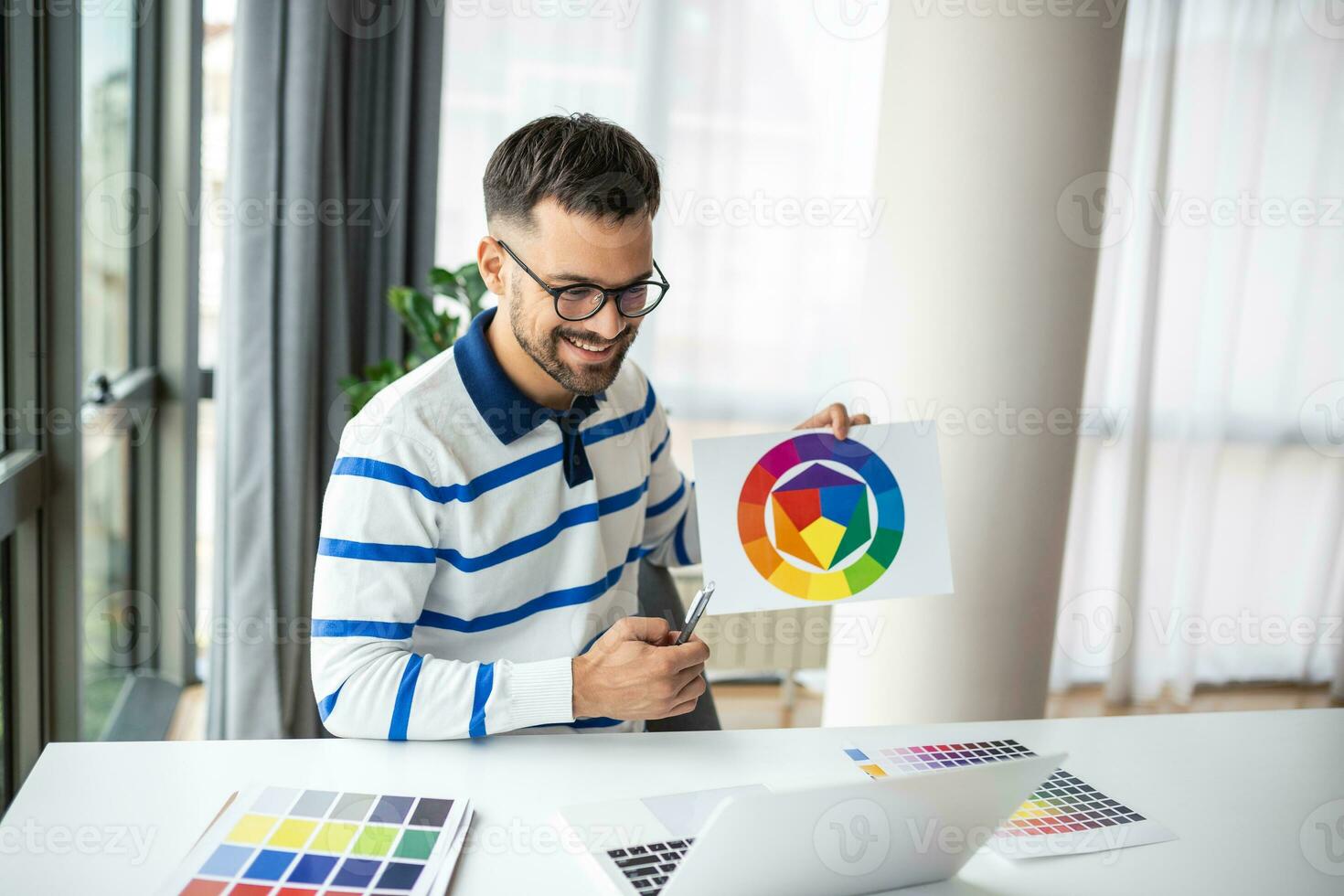 Young Freelance Graphic Designer Guy Working With Laptop And Color Swatches, Sitting At Desk In Home Office, Choosing Colour Gamma For New Design Project, Side View With Copy Space photo