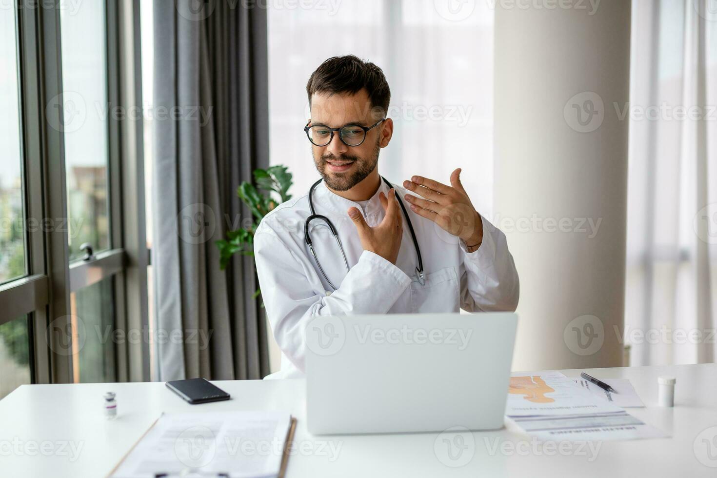 médico con ordenador portátil conduce un en línea vídeo llamada y negociaciones a paciente. masculino médico trabajando a oficina escritorio, oficina interior en antecedentes foto