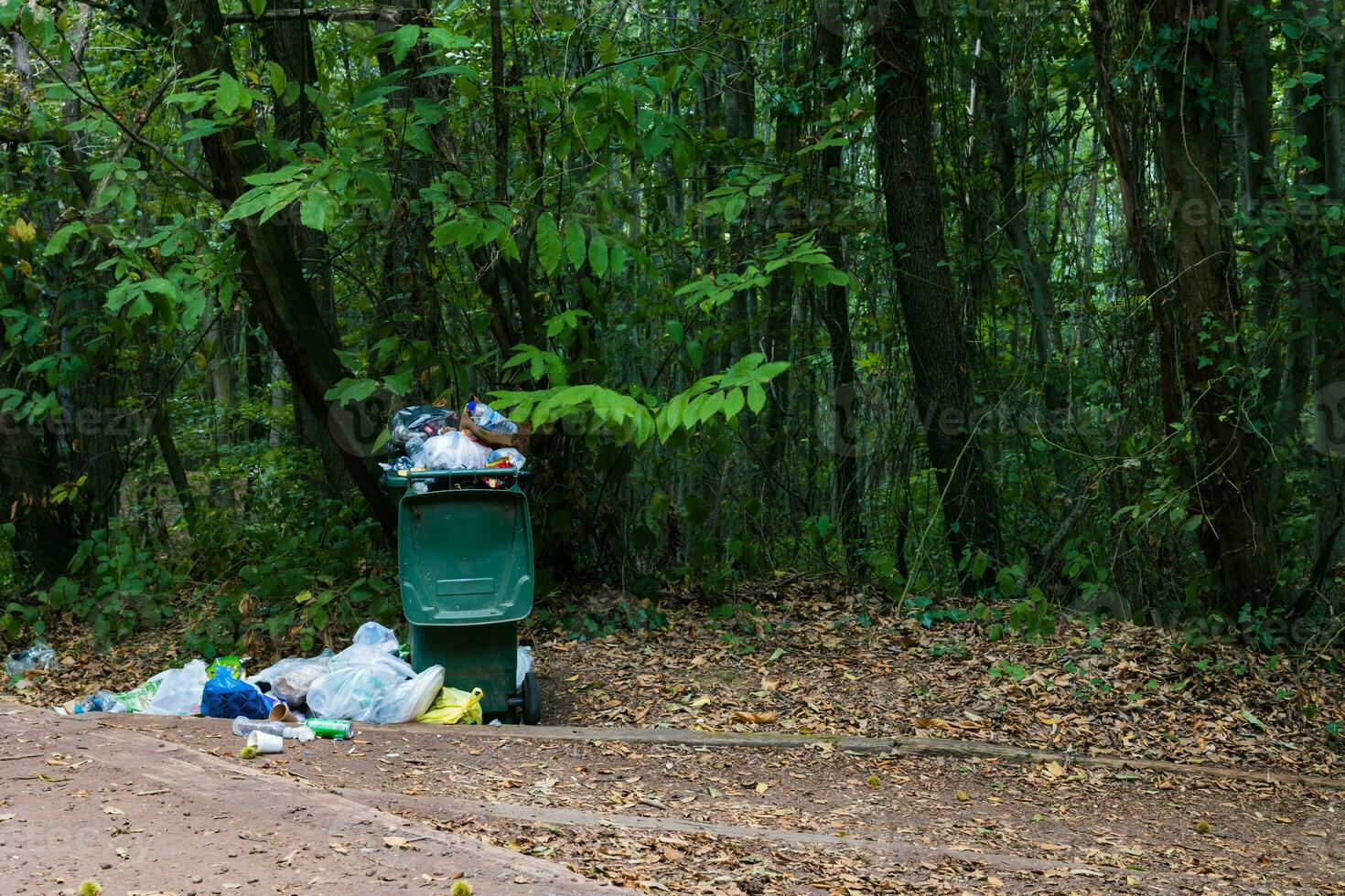 pile of garbage and a full trash bin in the forest. garbage pollution concept photo