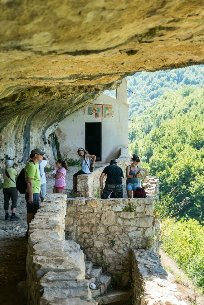 L'Aquila, Italy-august 12, 2021-People visit the Hermitage of San Bartolomeo an ancient church dug into a cliff with a well-preserved fresco, altar and hermit's cells. photo