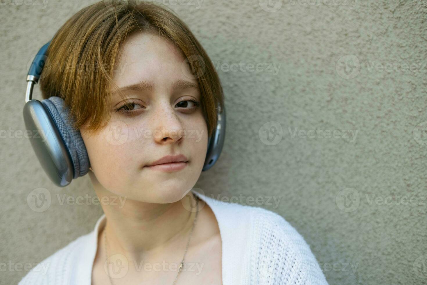 Portrait of a teenage girl in headphones against a gray wall. photo