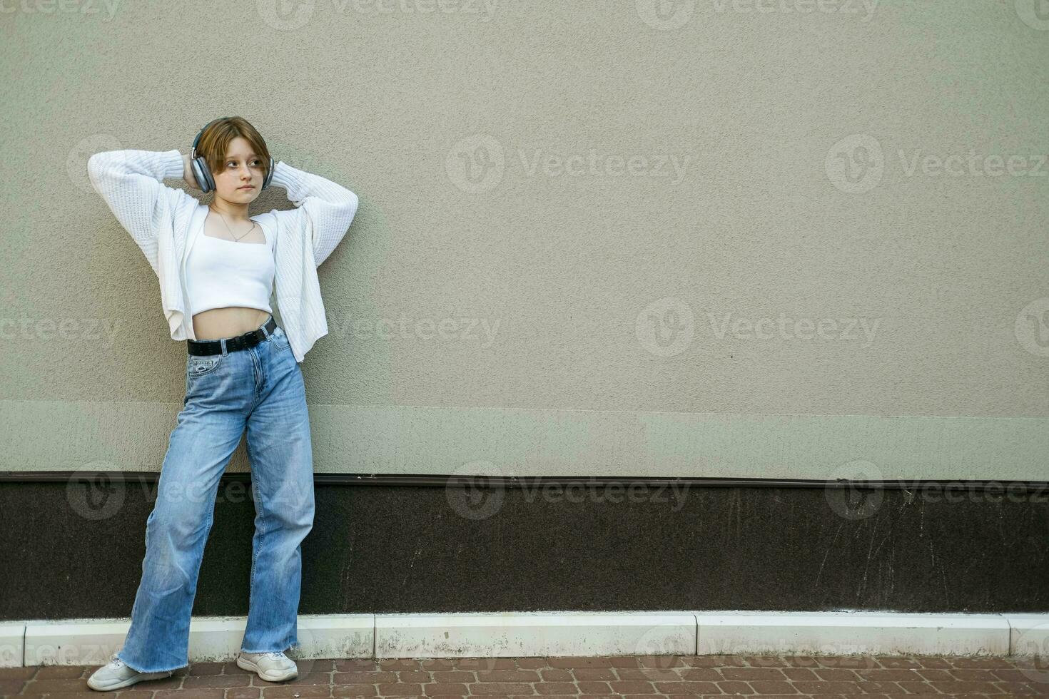 Portrait of a teenage girl in headphones against a gray wall. photo