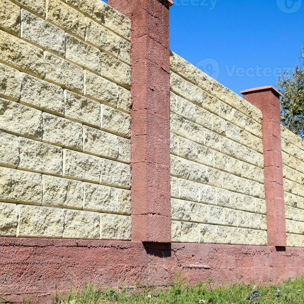 Fence made of bricks and decorative plaster. Yellow fence with red elements. High and beautiful fencing photo