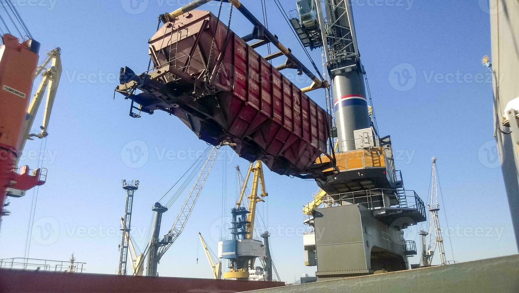 Moving freight railway car in the port by a port crane. Cargo lifting operations. Industrial port photo