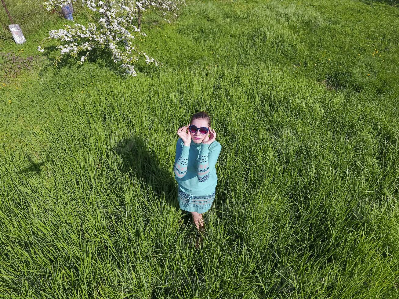 joven niña en un ligero verde vestir en el césped con verde césped. ver de un hombre desde encima desde un altura. foto