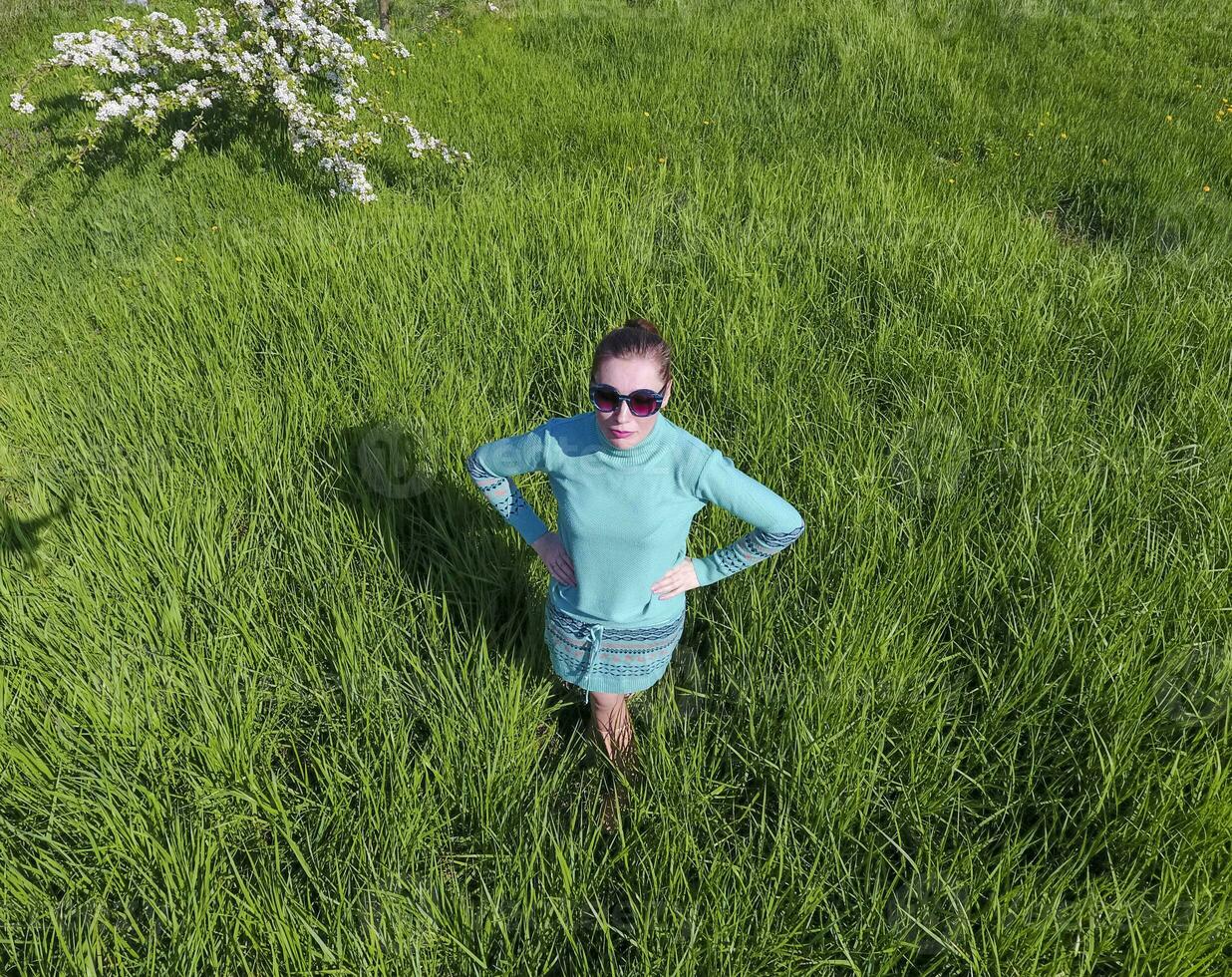 Young girl in a light green dress on the lawn with green grass. View of a man from above from a height. photo