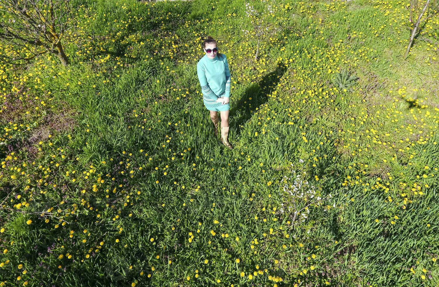 Young girl in a light green dress on the lawn with green grass. View of a man from above from a height. photo