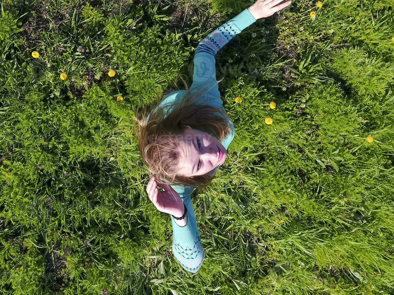 Young girl in a light green dress on the lawn with green grass. View of a man from above from a height. photo