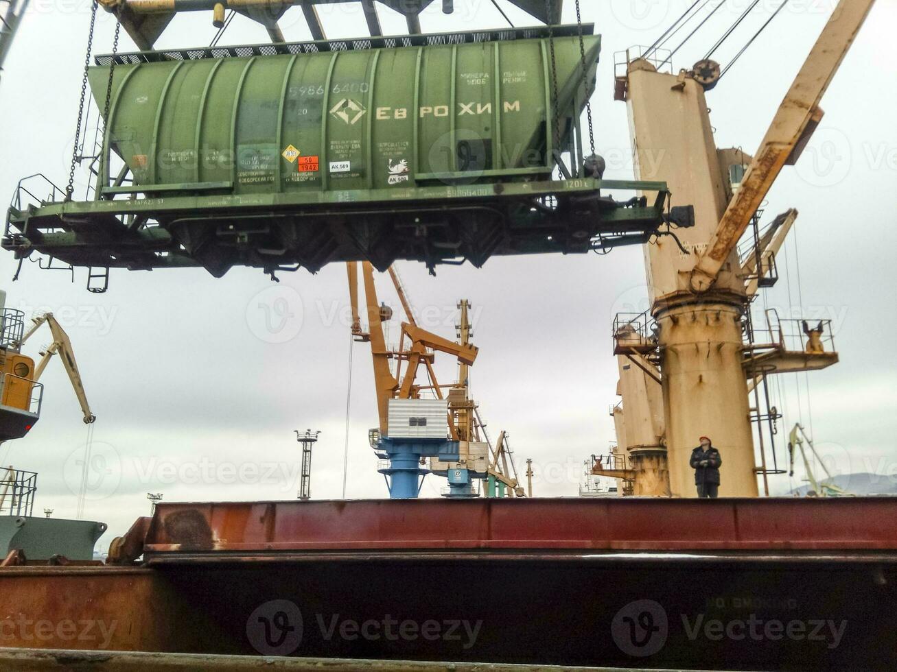 Moving freight railway car in the port by a port crane. Cargo lifting operations. Industrial port photo