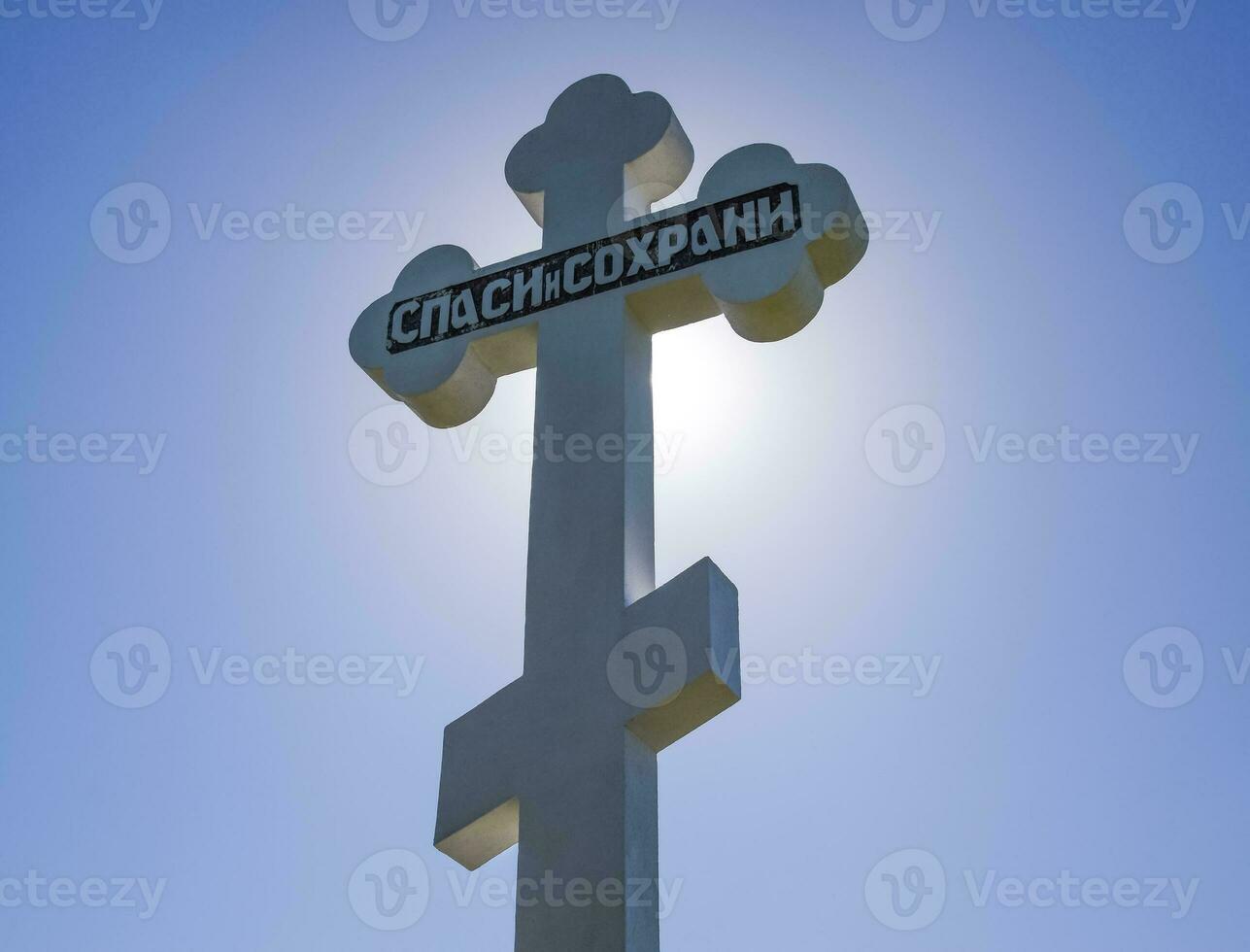 Orthodox cross against the blue sky and the sun. Cross in the ba photo