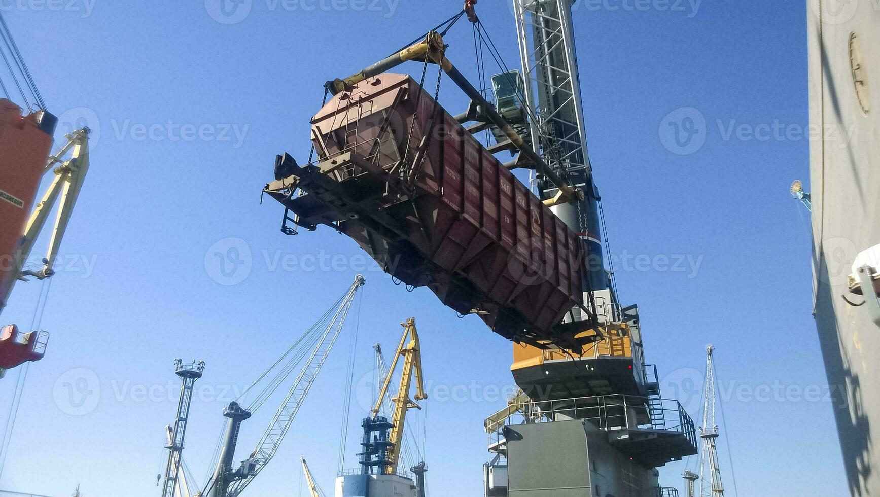 Moving freight railway car in the port by a port crane. Cargo lifting operations. Industrial port photo