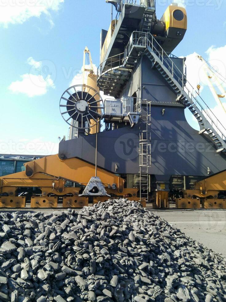 Piles of raw steel briquettes. Heap of coal anthracite in the port. Port cranes for coal loading photo