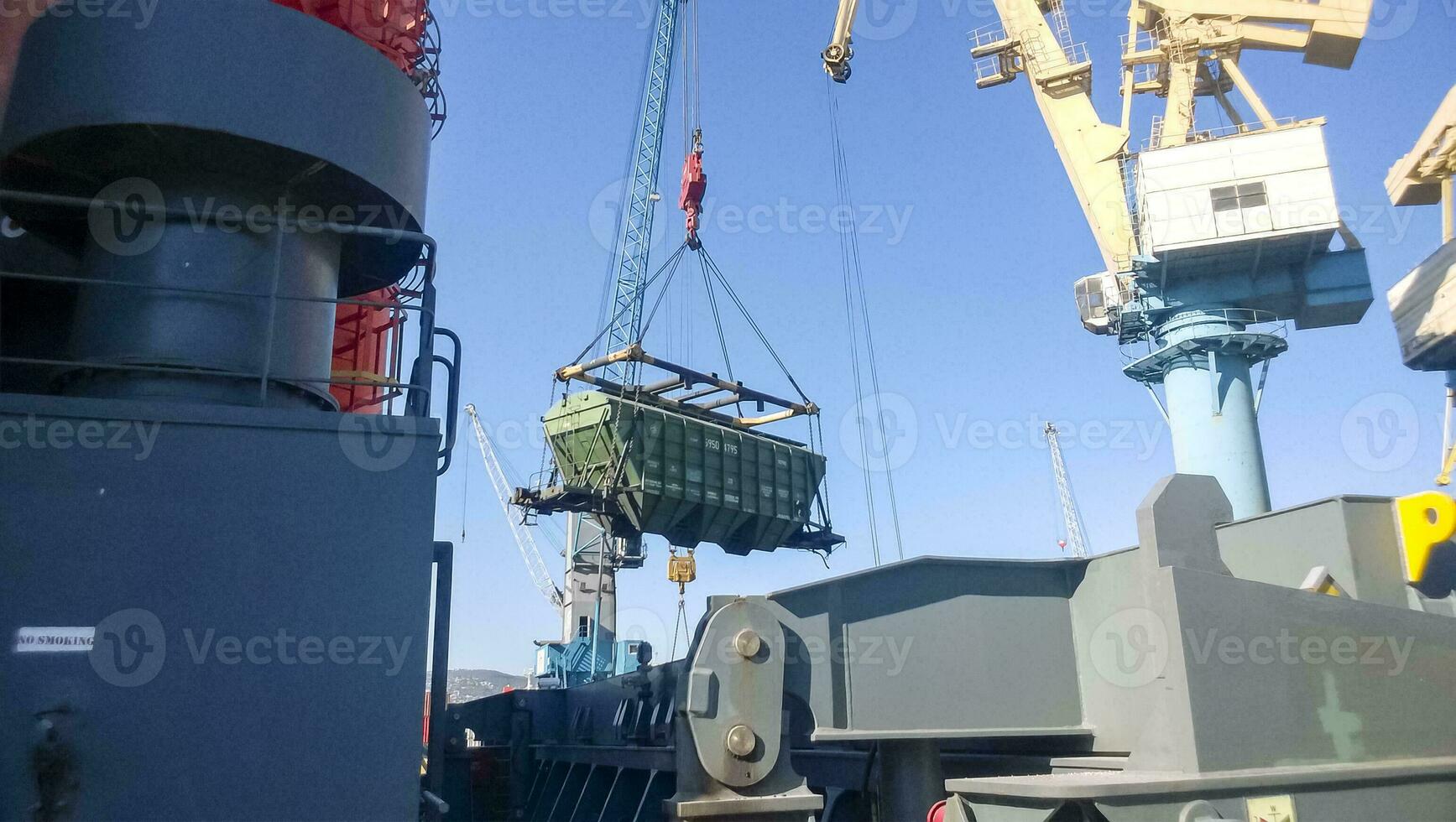 Moving freight railway car in the port by a port crane. Cargo lifting operations. Industrial port photo