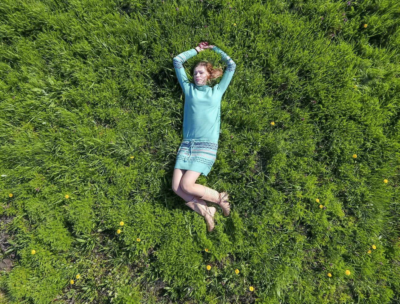 el niña mentiras en un turquesa vestir en el césped. hermosa niña acostado abajo de césped foto