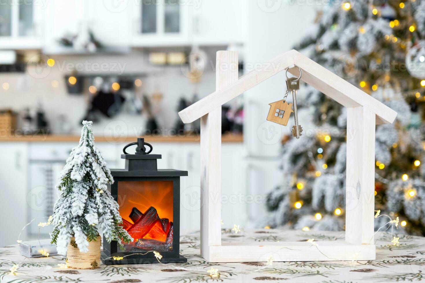 Key and tiny house of a small size on cozy home with Christmas decor on table of festive white kitchen. Gift for New Year. Insurance, moving to new house, mortgage, rent and purchase real estate photo