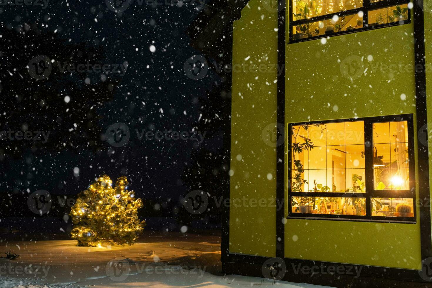 Cozy festive window of the house outside with the warm light of fairy lights garlands inside - celebrate Christmas and New Year in a warm home. Christmas tree, bokeh, snow on pine trees and snowfall photo