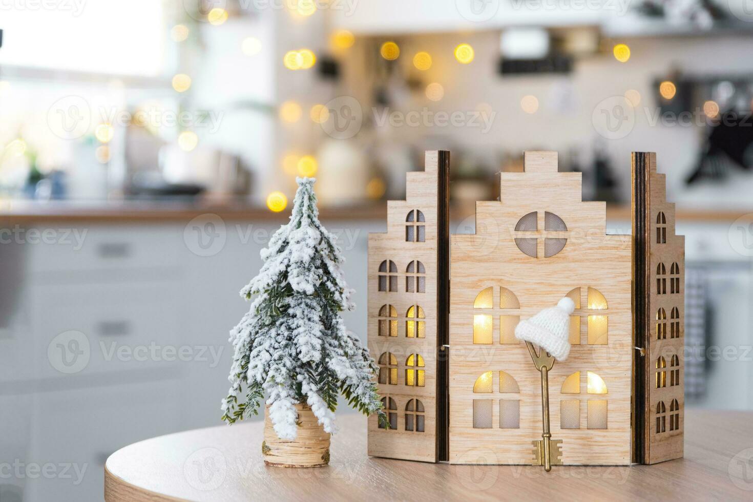 Key and tiny house of a small size on cozy home with Christmas decor on table of festive white kitchen. Gift for New Year. Insurance, moving to new house, mortgage, rent and purchase real estate photo