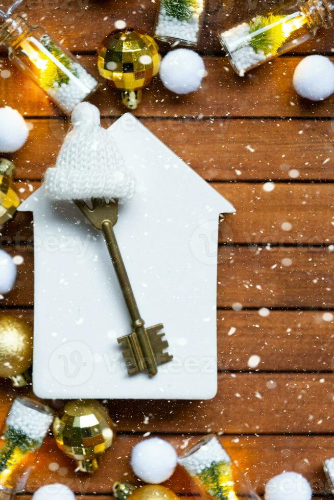 Key to house with a keychain tiny home on wooden background with Christmas decor layout. Gift for New Year, Christmas. Building, project, moving to new house, mortgage, rent and purchase real estate photo