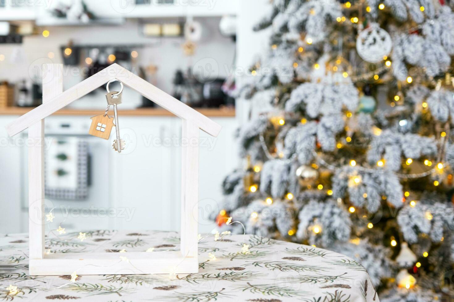 Key and tiny house of a small size on cozy home with Christmas decor on table of festive white kitchen. Gift for New Year. Insurance, moving to new house, mortgage, rent and purchase real estate photo