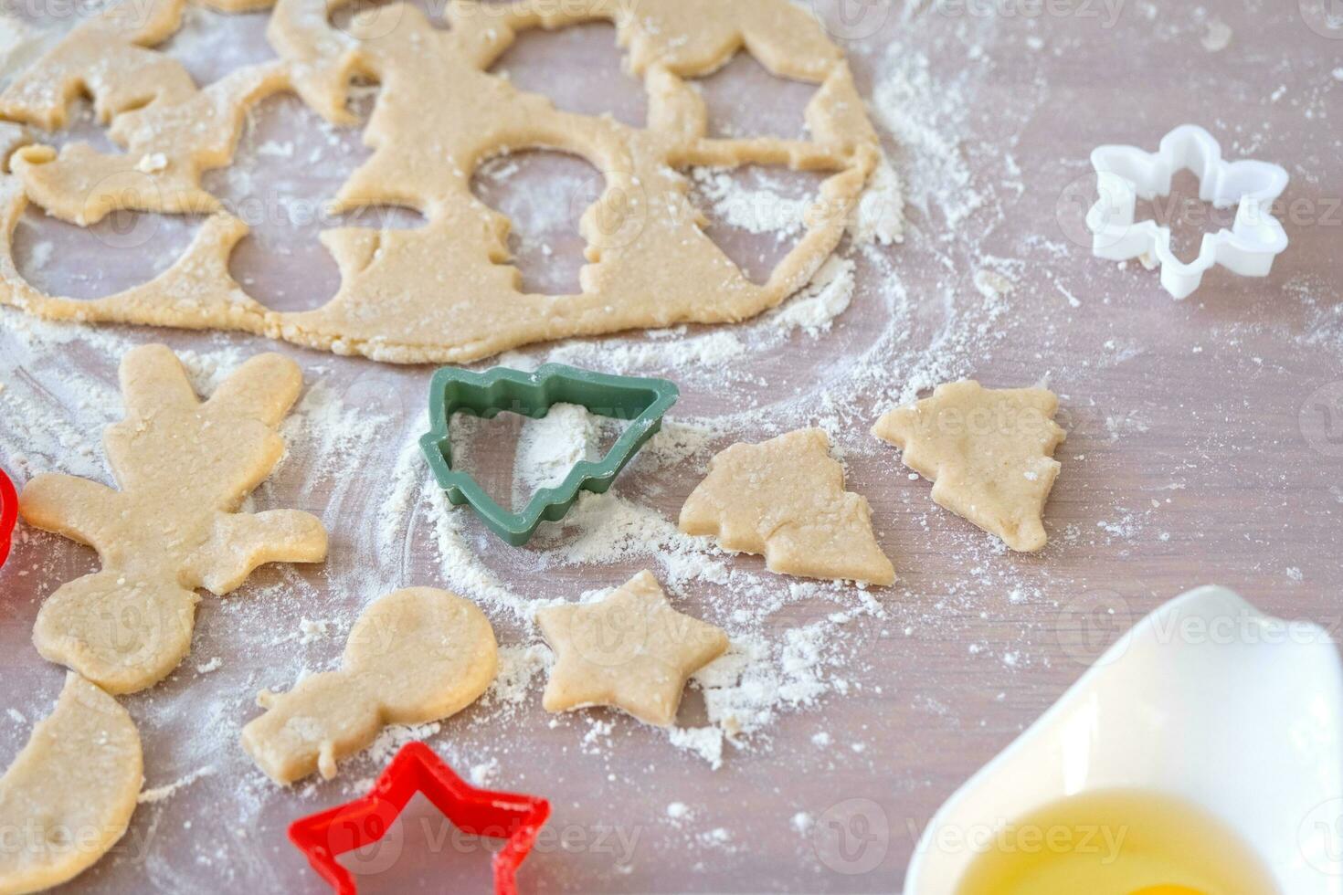 diseño de Galleta cortadores de cerca cortar fuera galletas desde el masa con moldes en un Navidad tema en el formar de un muñeco de nieve, un Navidad árbol, estrellas en el cocina foto