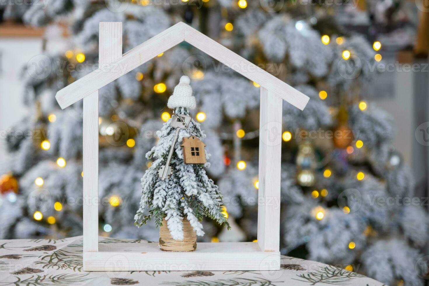 Key on Christmas tree and tiny house on cozy home with Christmas decor on table of festive white kitchen. Gift for New Year. Insurance, moving to new house, mortgage, rent and real estate photo
