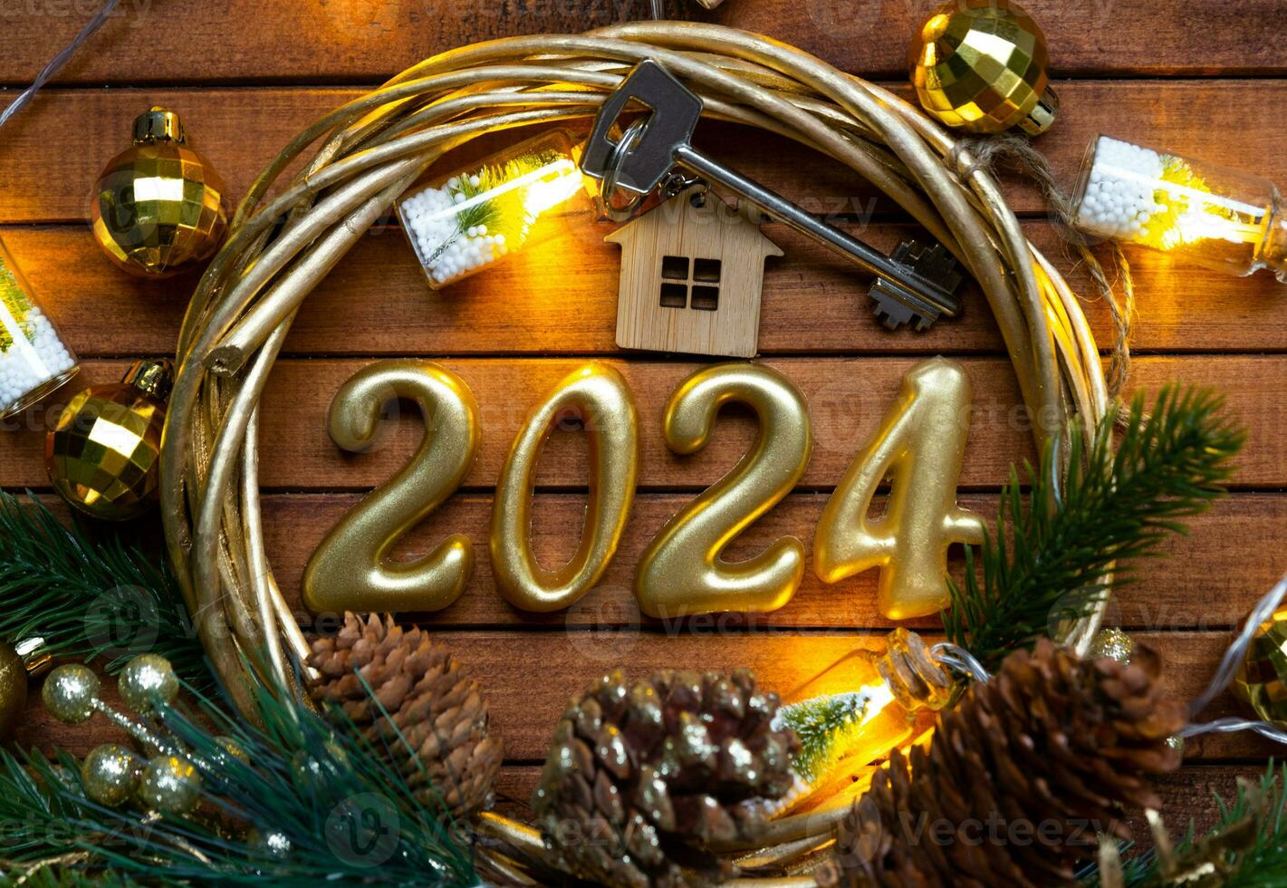 House key with keychain cottage on festive brown wooden background with stars, lights of garlands. New Year 2024 wooden letters, greeting card. Purchase, construction, relocation, mortgage, insurance photo