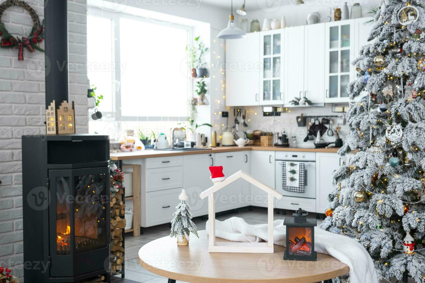 Christmas decor in white kitchen with burning stove fireplace, festive mess, village interior with a snowy Christmas tree. New Year, Christmas mood, cozy home. photo