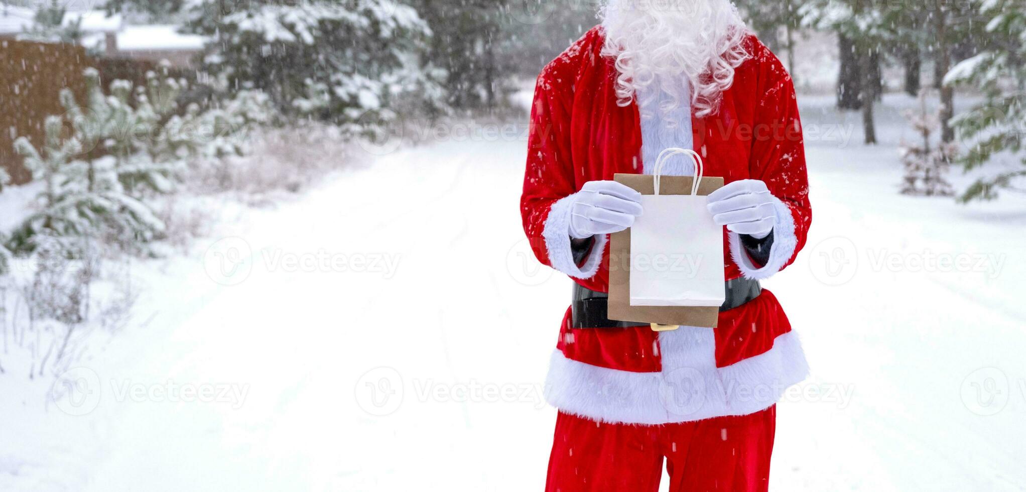 Santa Claus outdoor in winter and snow handing in hand eco paper bags with craft gift, food delivery. Shopping, packaging recycling, handmade, delivery for Christmas and New year photo