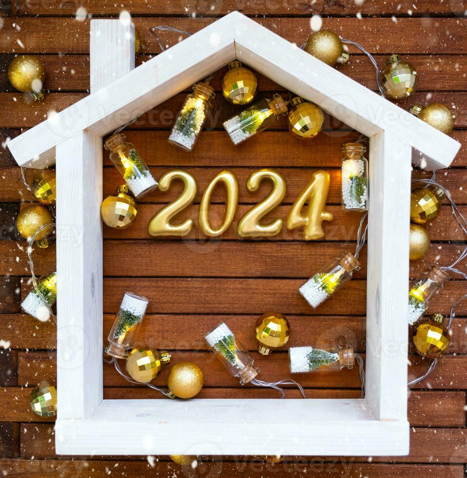 House key with keychain cottage on festive brown wooden background with stars, lights of garlands. New Year 2024 wooden letters, greeting card. Purchase, construction, relocation, mortgage, insurance photo