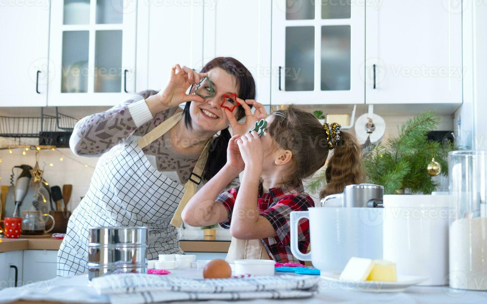 Mom and daughter in the white kitchen are preparing cookies for Christmas and new year. Family day, preparation for the holiday, learn to cook delicious pastries, they hold cookie cutters like glasses photo
