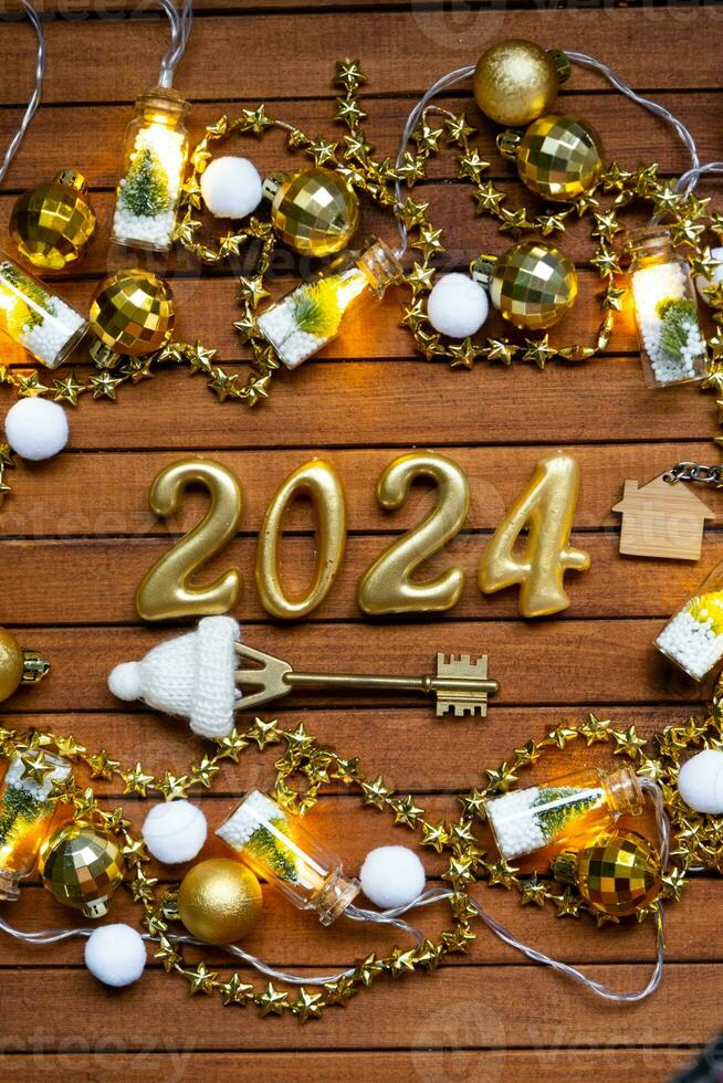 House key with keychain cottage on festive brown wooden background with stars, lights of garlands. New Year 2024 wooden letters, greeting card. Purchase, construction, relocation, mortgage, insurance photo