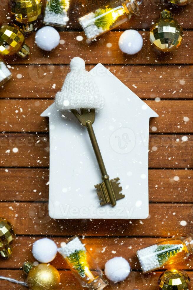 Key to house with a keychain tiny home on wooden background with Christmas decor layout. Gift for New Year, Christmas. Building, project, moving to new house, mortgage, rent and purchase real estate photo