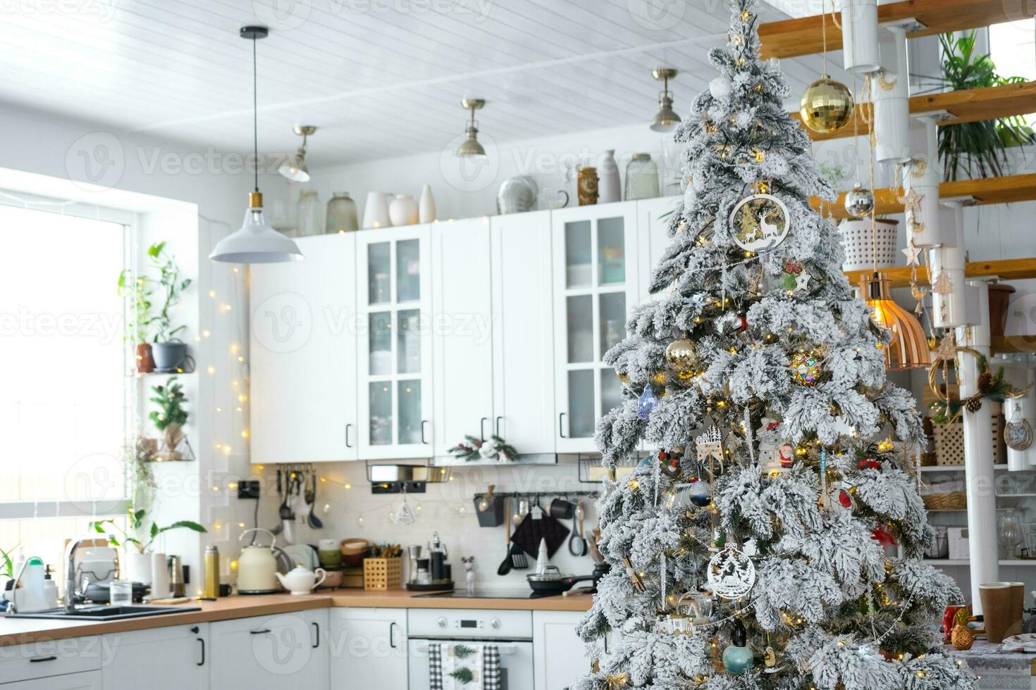 Festive Christmas decor in white kitchen, modern village interior with a snowy Christmas tree and fairy lights. New Year, Christmas mood, cozy home, Metal modular staircase. The general plan photo